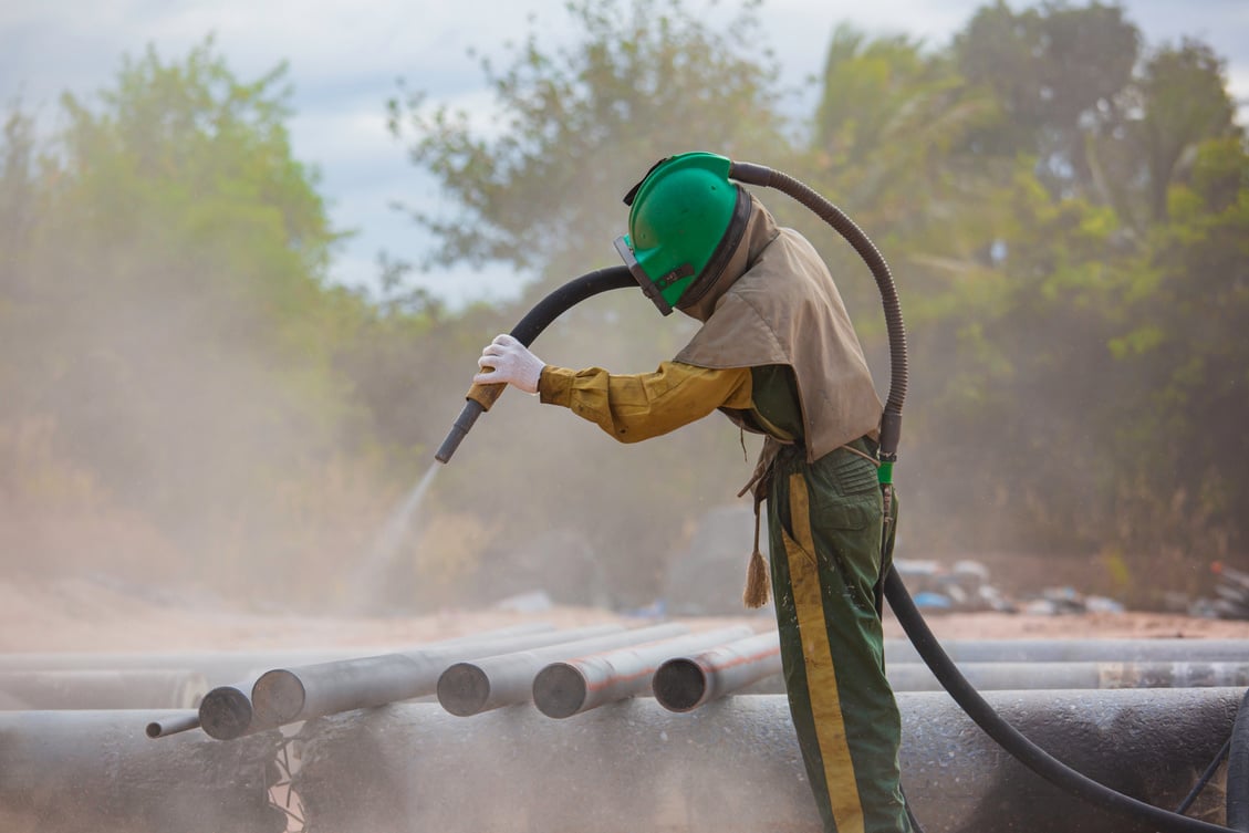 Worker Sandblasting Metal Pipes